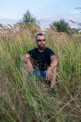 A young man with a beard and a mohawk in a field at sunset.