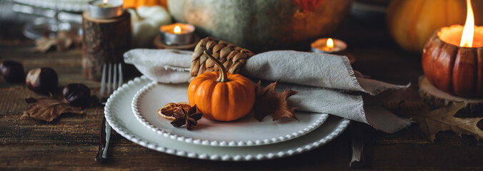 Cozy festive holiday table decor, home family Thanksgiving dinner. Traditional event, elegant natural rustic decoration. Countryside style. Burning candles, floral centrepiece pumpkin banner