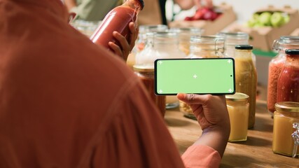 Canvas Print - African american woman shows greenscreen looking at organic natural bulk products placed in reusable jars. Customer checks smartphone app with isolated chromakey display.