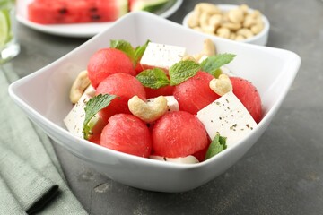 Delicious watermelon salad with feta cheese, cashew nuts and spices in bowl on grey textured table, closeup