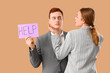 © Pixel-Shot - Business man holding paper with word HELP and his female colleague on beige background. Harassment concept