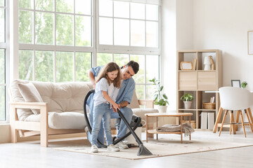 Canvas Print - Young father and his daughter with vacuum cleaner cleaning carpet together at home