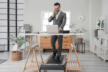 Poster - Handsome businessman talking by mobile phone on treadmill at table in office