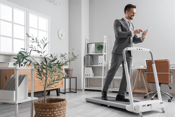 Canvas Print - Handsome businessman working with tablet computer on treadmill in office