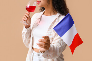 Poster - Beautiful young happy African-American woman with flag of France and glass of red wine on beige background, closeup