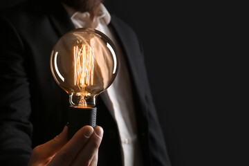 Wall Mural - Businessman holding glowing light bulb on black background, closeup