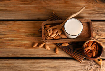 Wall Mural - Glass of fresh almond milk and bowl with nuts on wooden background