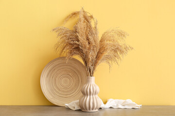 Poster - Vase with dry reeds and plate on table against color wall