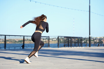 Wall Mural - Beautiful young Asian woman jogging along waterfront promenade outdoors, back view