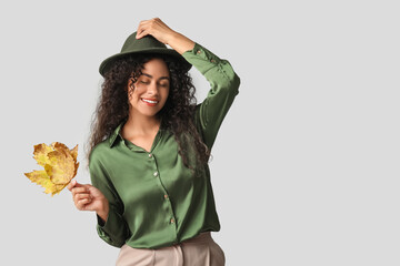 Wall Mural - Beautiful young happy African-American woman in stylish outfit with autumn leaves on grey background