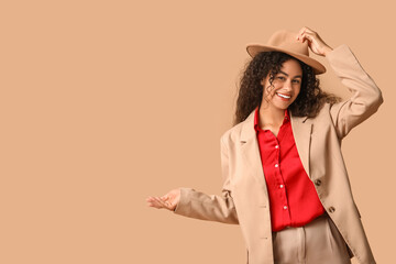 Beautiful young happy African-American woman in stylish suit pointing at something on beige background