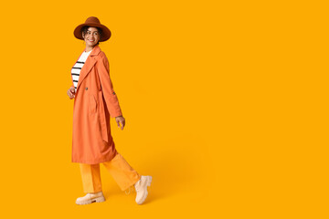 Poster - Beautiful young happy African-American woman in autumn outfit on orange background