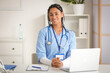© Pixel-Shot - Young African-American female doctor with laptop sitting at table in clinic