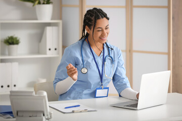 Wall Mural - Young African-American female doctor with laptop working at table in clinic