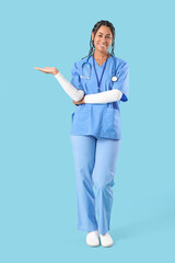 Poster - Young African-American female doctor with stethoscope showing something on blue background