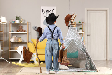 Wall Mural - Cute little cowboy with toy horse and boots at home, back view