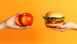 © Andrii Fanta - One hand holding apple fruit other holding hamburger, orange background