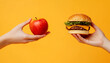 © Andrii Fanta - One hand holding apple fruit other holding hamburger, orange background