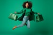 © useful pictures - Very excited african american young adult woman happy jumping with shopping bags on green background. Payday delight. Studio portrait of cheerful girl carrying shoppers jumping for joy. Christmas Sale