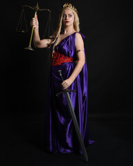 Wall Mural - Close up portrait of beautiful blonde female model wearing silk grecian toga dress, holding justice scales, historical fantasy goddess. isolated dark studio background.