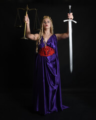 Poster - Close up portrait of beautiful blonde female model wearing silk grecian toga dress, holding justice scales, historical fantasy goddess. isolated dark studio background.