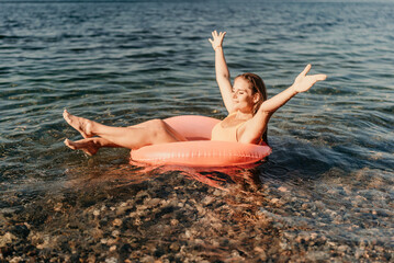 Wall Mural - A woman is floating on a pink inflatable raft in the ocean. The water is calm and the sky is clear. The woman is enjoying her time in the water.