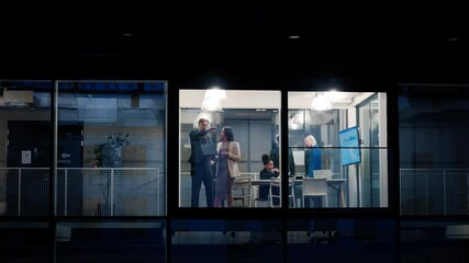 Aufkleber - Footage from the Street at Night: Businesswoman and Businessman in a Suit Using a Laptop Computer in the Office. Managers Standing by the Window. Employees Talk About a Financial Development Deal