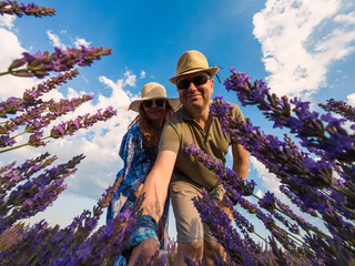 Couple in Hats Taking Selfie Among Lavender Bushes Against Blue Sky