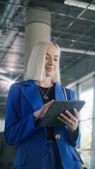 Poster - Vertical Screen: Young Businesswoman Smiling While Checking Financial Documents on a Tablet Computer. Portrait of a Successful Female Corporate Manager Walking in a Spacious Modern Office Building