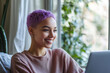 © Mina - Portrait of happy mixed race woman with short purple hair sitting at home using laptop