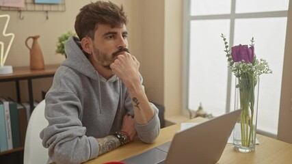 Wall Mural - Pensive bearded man with tattoos working on laptop in bright home interior.