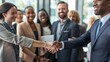 © liliyabatyrova - A diverse group of professionals is gathered in an office setting, with two individuals shaking hands to establish a business connection. The atmosphere is friendly and welcoming