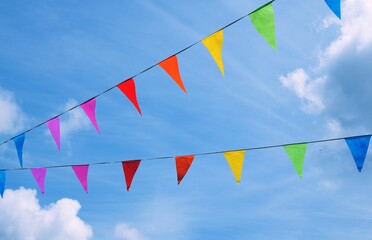 Colorful triangular pennant flags or bunting flags strung across a blue sky with clouds 