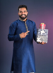 Young happy smiling handsome man holding gift box and posing on dark background