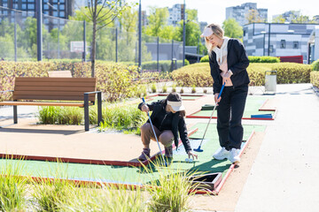 Wall Mural - mother and daughter playing mini golf, children enjoying summer vacation