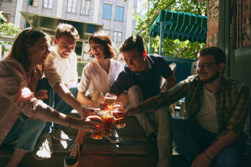 Sunny summer day vibes. Happy young people, men and women, friends gathering at local outdoor pub, bar to drinking refreshing beer. Relaxation and joy. Concept of relaxation, party, beer