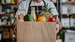 © liliyabatyrova - A person holds a cardboard box filled with fresh fruits, vegetables, and beverages while standing in a market, showcasing the convenience of home delivery services