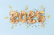 © rorygezfresh - 2025 New Year holidays concept. Golden inflatable balloons, ribbons and glittering stars confetti on a blue background.