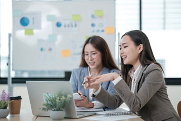 Wall Mural - Two women are sitting at a table with a laptop and a whiteboard