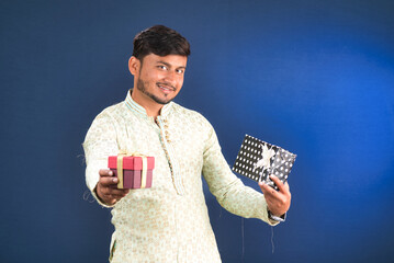 Young happy smiling handsome man holding gift box and posing on dark background