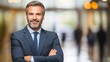 © Iswanto - Portrait of a confident businessman with a friendly smile, arms crossed, standing in a modern office building.