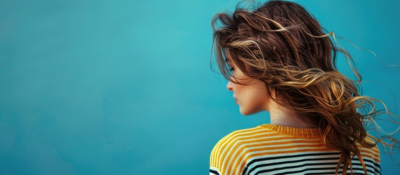 A woman with wavy hair in a fashionable striped sweater is set against a blue background with blank space for text expressing the Break The Bias concept. Copy space image