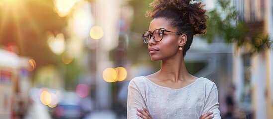 An attractive confident African American woman stands outside on the street deep in thought with her arms crossed and hands touching displaying a chic demeanor as she plans her ideas There is copy sp