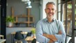 © JINGWEN - Smiling handsome businessman with crossed arms in modern office, middle-aged gray-haired man exuding confidence, business success concept.