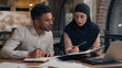 © Yuliia - Two business colleagues muslim islamic businesswoman in hijab Arabian businessman working with laptop together in office woman coach talk consult explain teach advice trainee man writing in notebook