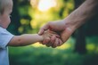 © StockUp - Father holds a child's hand in a heartwarming gesture, set against a backdrop of lush greenery in natural sunlight.