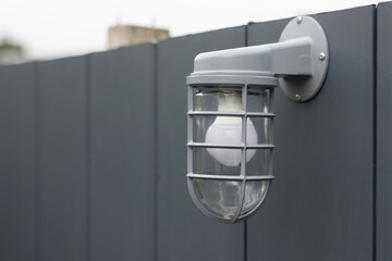 Wall Mural - A light fixture with a white bulb is hanging from a gray fence