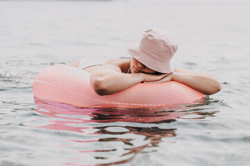 Canvas Print - A woman is laying on a pink inflatable raft in the ocean. The scene is peaceful and relaxing, with the woman enjoying the water and the sun.