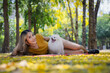 © kamonrat - Woman Lying on the Ground with a Happy Pomeranian Dog Surrounded by Yellow Leaves in a Lush Green Park on a Bright Day