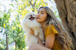 © kamonrat - Woman Sharing a Loving Kiss with Her Pomeranian in a Tranquil Park, Surrounded by Vibrant Nature and Sunshine